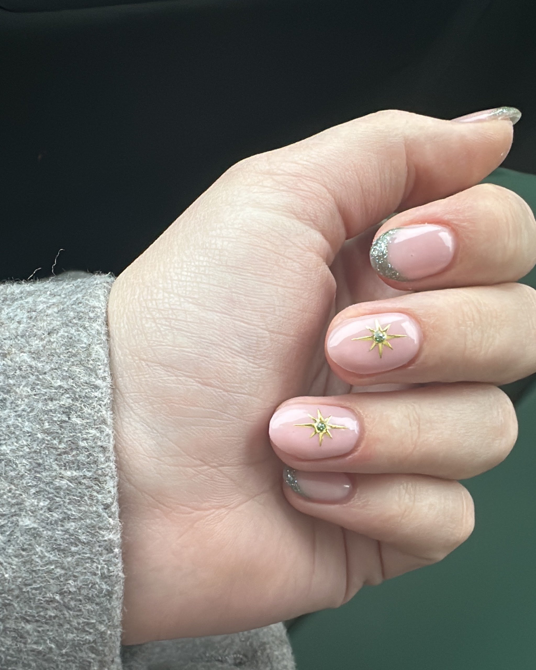 Hand met zachtroze nagels met kleine gouden accenten en een zilveren glittertip